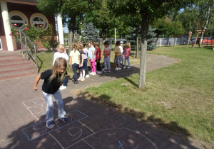 dzieci bawią się o ogrodzie przedszkolnym w piękny słoneczny dzień, grają w klasę